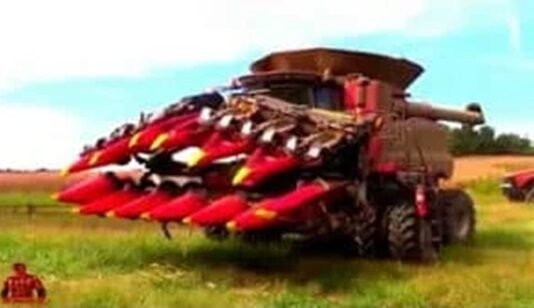 A large red harvester with front attachments sits in a field, showcasing the latest in farming technology and ready for work.