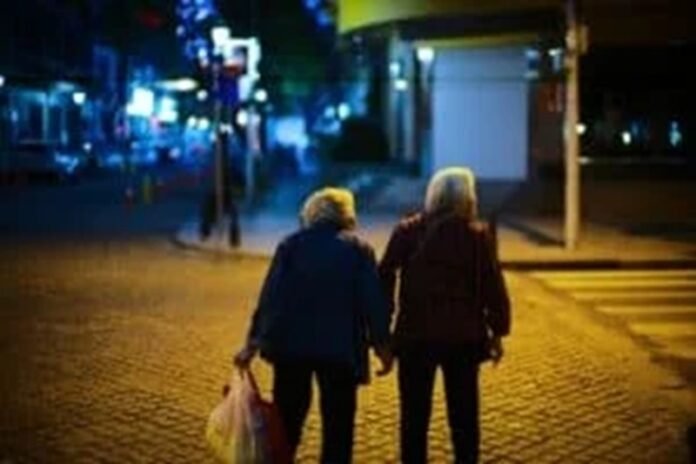 Two elderly people walk hand in hand on a dimly lit street at night, with one carrying a plastic bag, savoring these tender moments as though they were your last days. Two elderly people walk hand in hand on a dimly lit street at night, with one carrying a plastic bag, savoring these tender moments as though they were your last days.