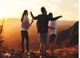 How Does Your Life Shape Your Age? Four people stand on a hilltop at sunset, arms raised, overlooking a scenic view. How does your life shape your age
