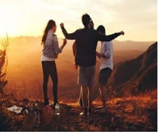 Four people stand on a hilltop at sunset, arms raised, overlooking a scenic view. How does your life shape your age Four people stand on a hilltop at sunset, arms raised, overlooking a scenic view. How does your life shape your age