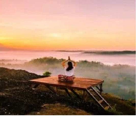 Person meditating on a wooden platform overlooking a misty valley at sunrise, finding peace of mind amidst the serene beauty.
