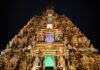 An ornate Hindu temple is lit up at night, attracting visitors on their temple visits.