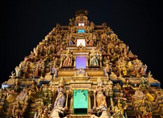 An ornate Hindu temple is lit up at night, attracting visitors on their temple visits.