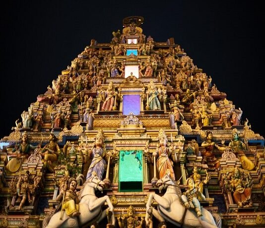 An ornate Hindu temple is lit up at night, attracting visitors on their temple visits.