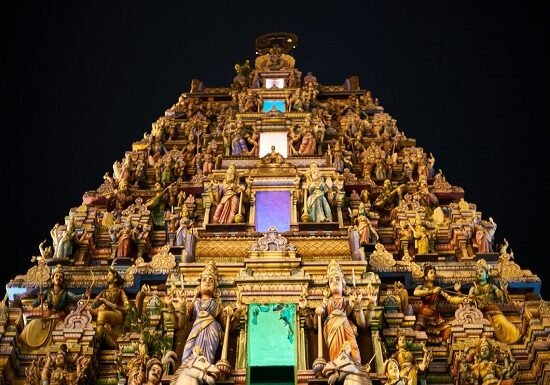 An ornate Hindu temple is lit up at night, attracting visitors on their temple visits.