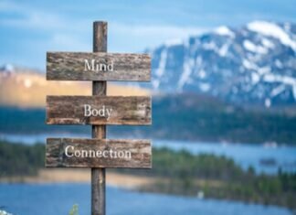 A wooden sign with "Mind," "Body," "Connection" stands gracefully against a serene lake and mountain backdrop, capturing the essence of natural health.