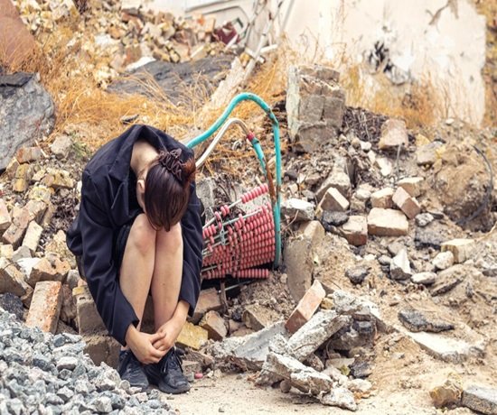 A person sits hunched over amidst rubble and debris, remnants of an earthquake bomb or airstrike, with hoses and broken bricks scattered in the background. A person sits hunched over amidst rubble and debris, remnants of an earthquake bomb or airstrike, with hoses and broken bricks scattered in the background.