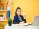 A person sits at a desk, holding a cup and writing in a notebook. A laptop, a plant, shelves with books, and freelance jobs for beginners with no experience